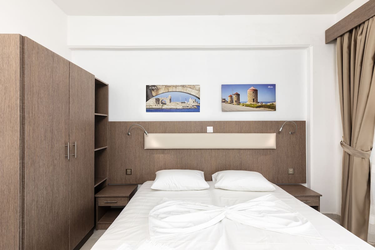 Una habitación de hotel con una cama, un armario, una mesita de noche y dos cuadros en la pared.
