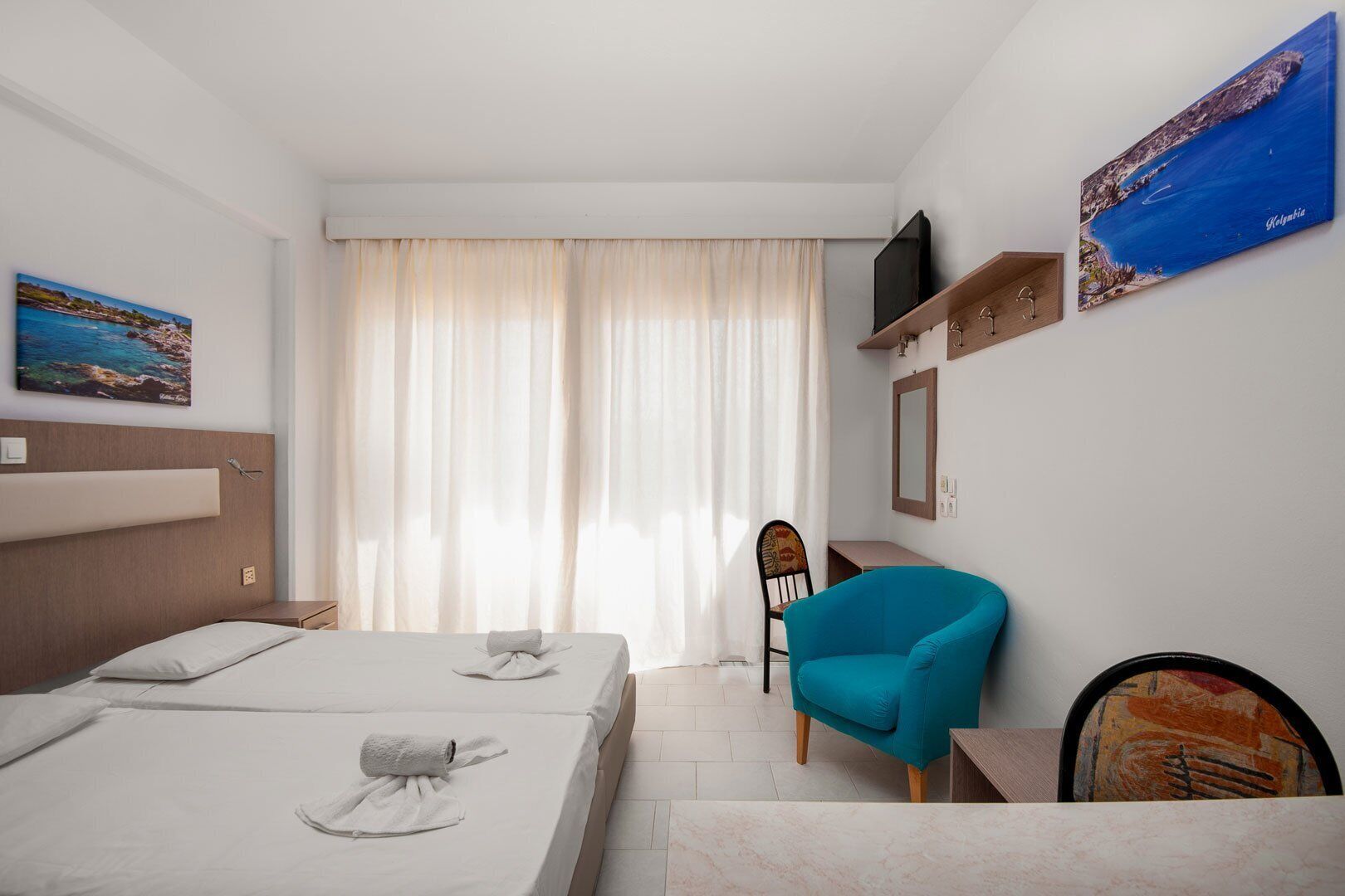 Una camera d'albergo con due letti, una scrivania, una sedia, una televisione e opere d'arte alle pareti.