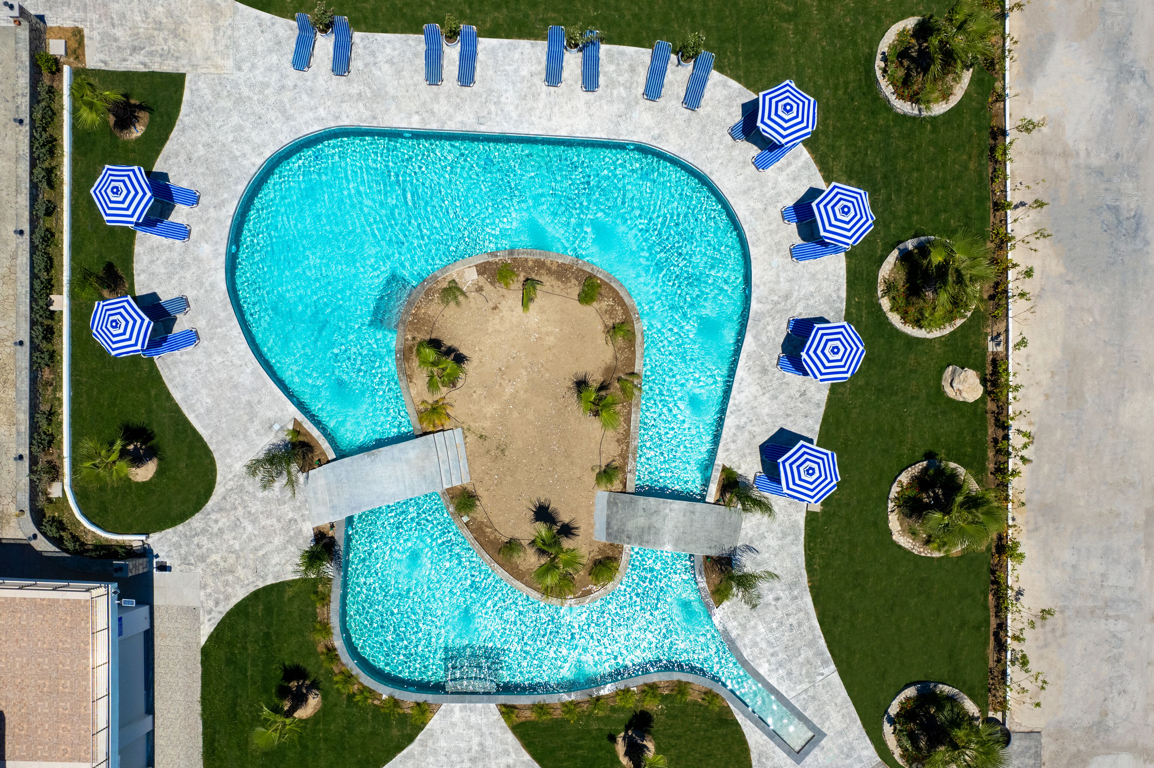 Una piscina grande con un centro arenoso, rodeada de sillas de descanso y sombrillas.