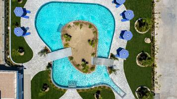 Una piscina grande con un centro arenoso, rodeada de sillas de descanso y sombrillas.