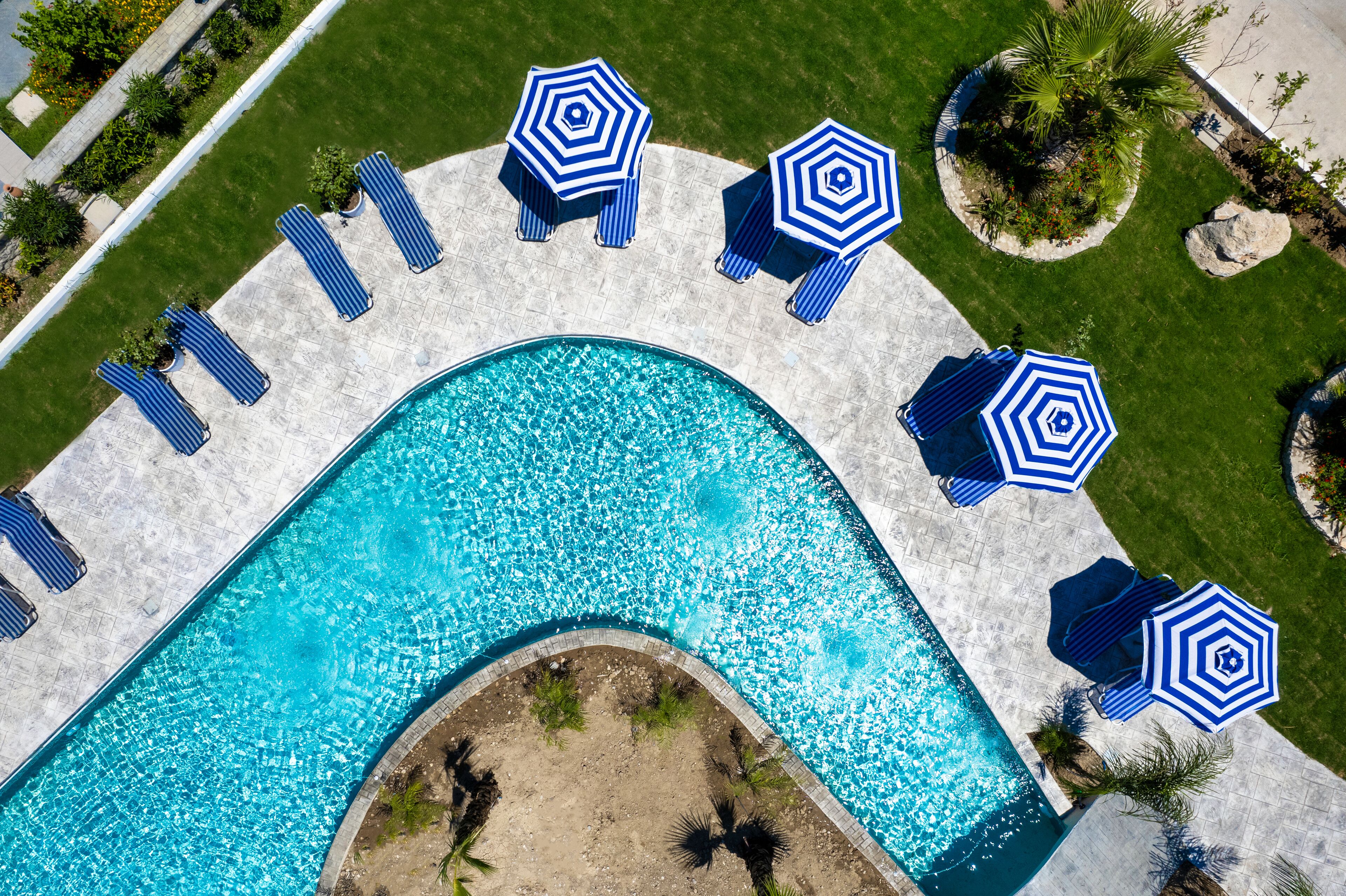 Vista aerea di una piscina con ombrelloni blu e lettini disposti intorno.