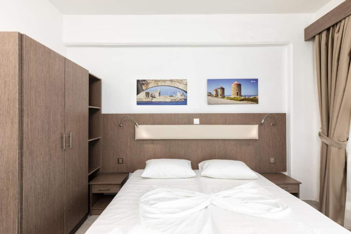 Una habitación de hotel con cama, armario, mesita de noche y dos cuadros en la pared.