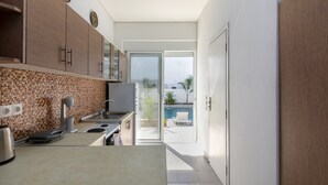 A modern kitchen with a tiled backsplash, a built-in oven, and a view of a swimming pool through a glass door. - Paradise Garden (Rhodes)