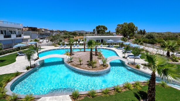 A large, curved swimming pool with lounge chairs and umbrellas, surrounded by palm trees and greenery. - Paradise Garden (Rhodes)