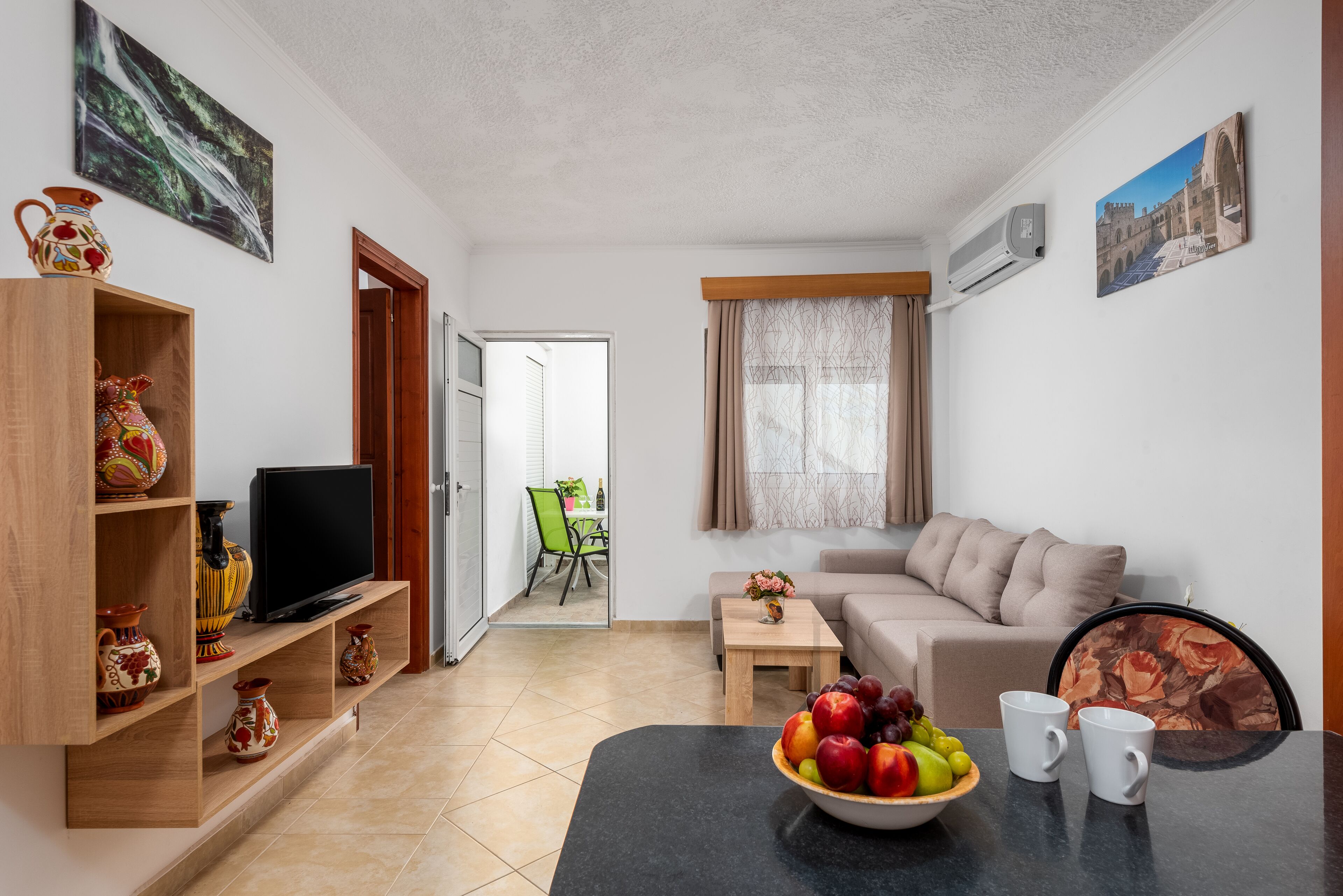 A living room with a sofa, TV, and a dining table with fruit and cups.