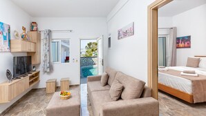 A modern, well-lit room with a sofa, a bed, a TV, and a small table with fruit. - Paradise Garden (Rhodes)
