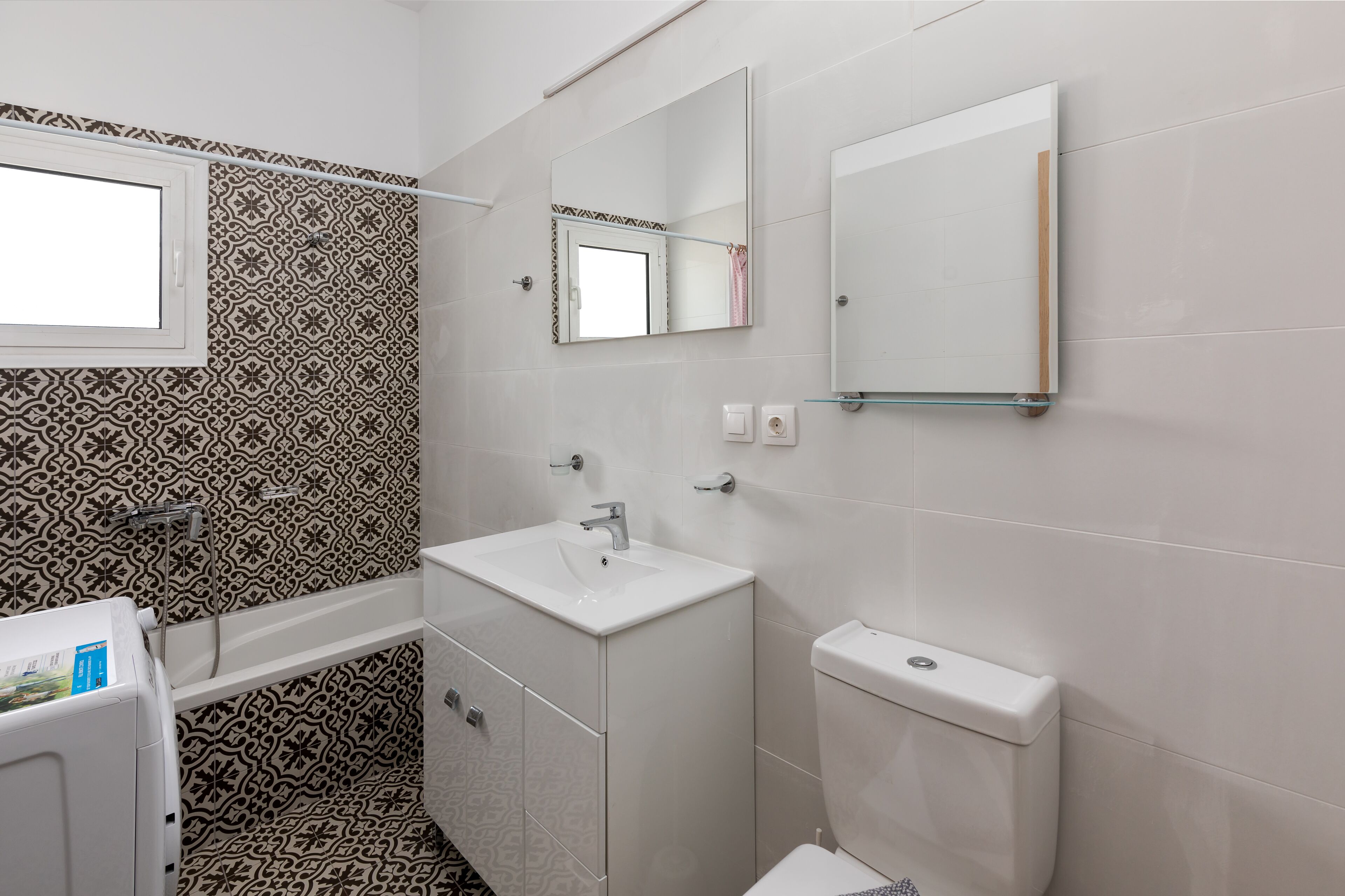 A bathroom with patterned tiles, a white sink, a mirror, and a toilet.