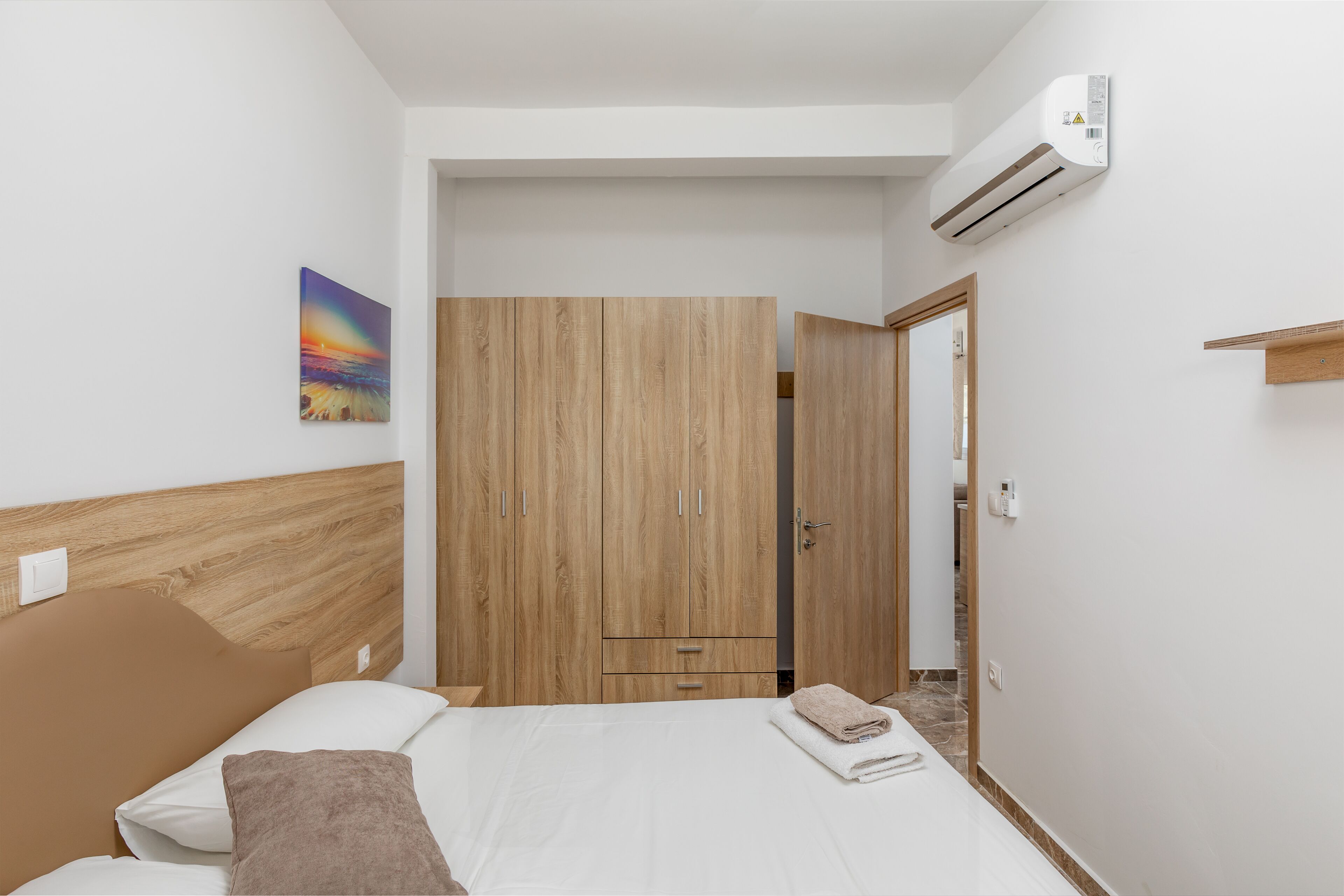 A bedroom with a bed, wooden wardrobe, and an air conditioning unit.