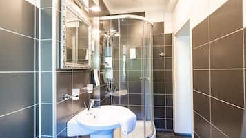 A modern bathroom with a curved glass shower enclosure, a white sink with a towel, and a large mirror.