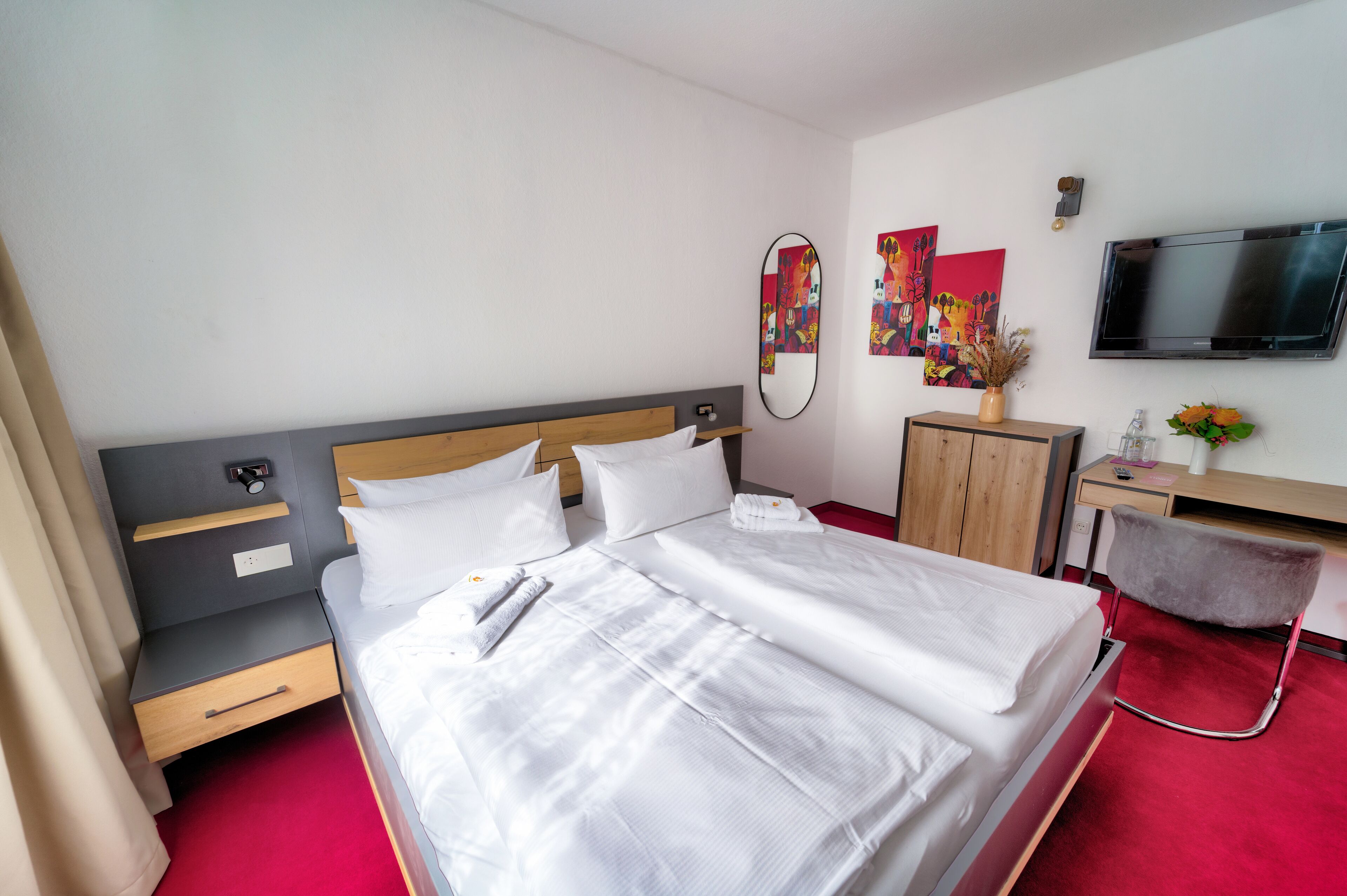 Una habitación de hotel con una cama grande, un escritorio, una silla, un televisor y obras de arte en las paredes.