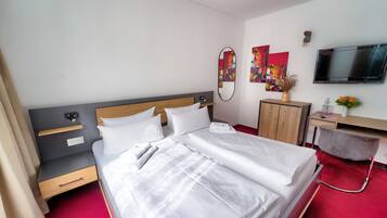 Una habitación de hotel con una cama grande, un escritorio, una silla, un televisor y obras de arte en las paredes.