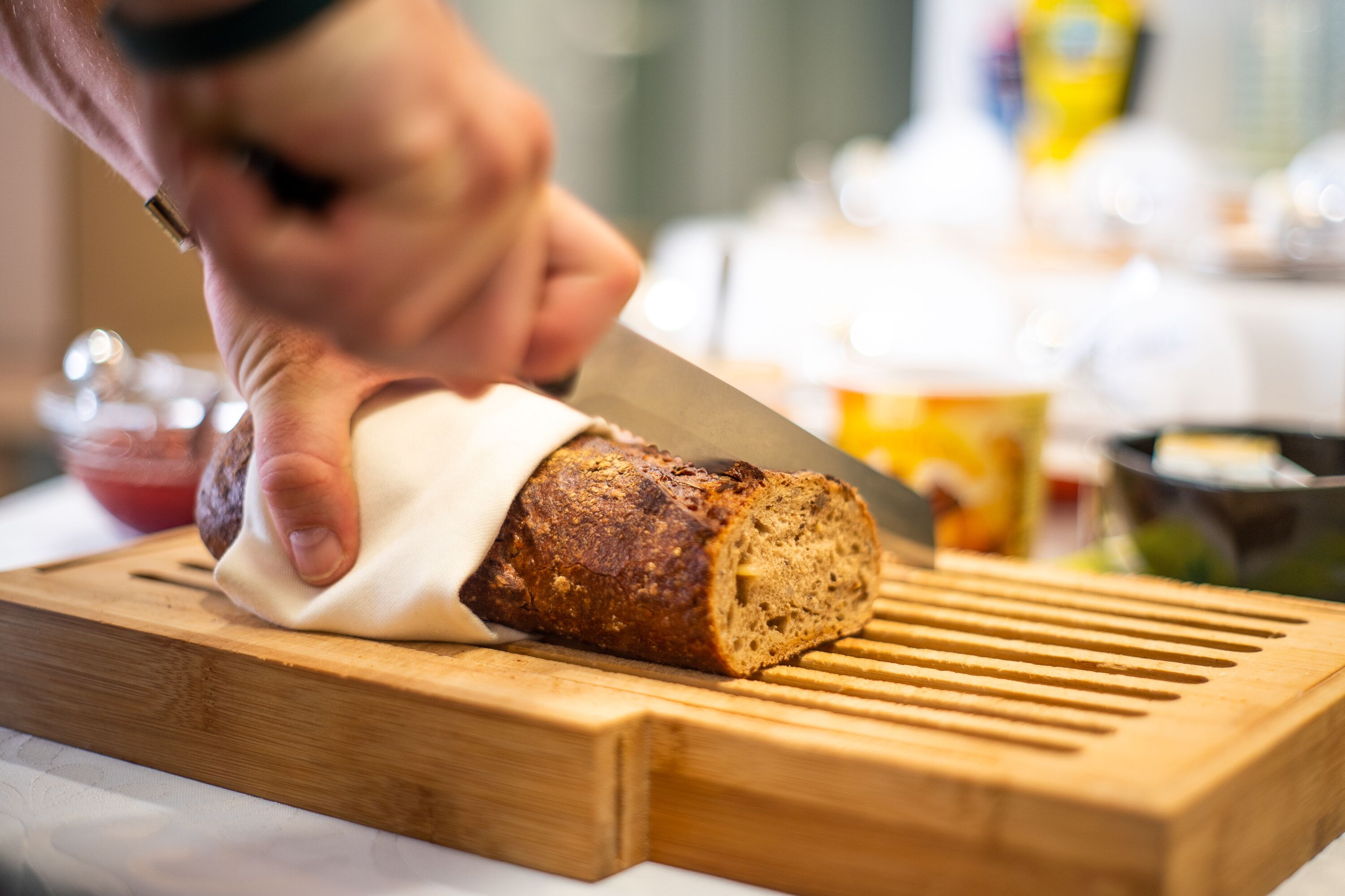 A loaf of bread being sliced on a wooden cutting board.