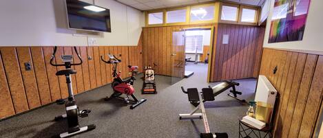 Un gimnasio con equipamiento de ejercicio, televisión y paneles de madera.