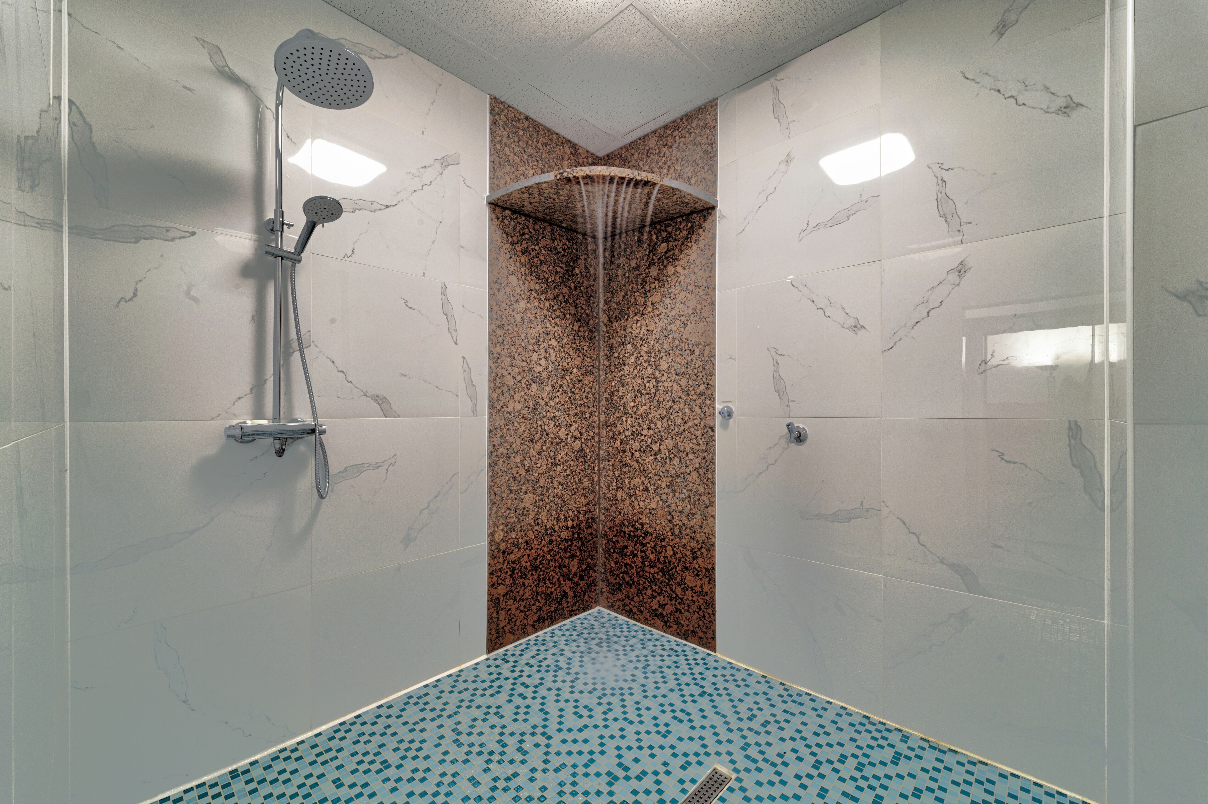 A shower with a rain showerhead, a handheld showerhead, and a floor with a blue and white pattern.