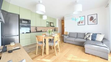 A modern kitchen with green cabinets, a stainless steel refrigerator, and a dining area with a wooden table and chairs.