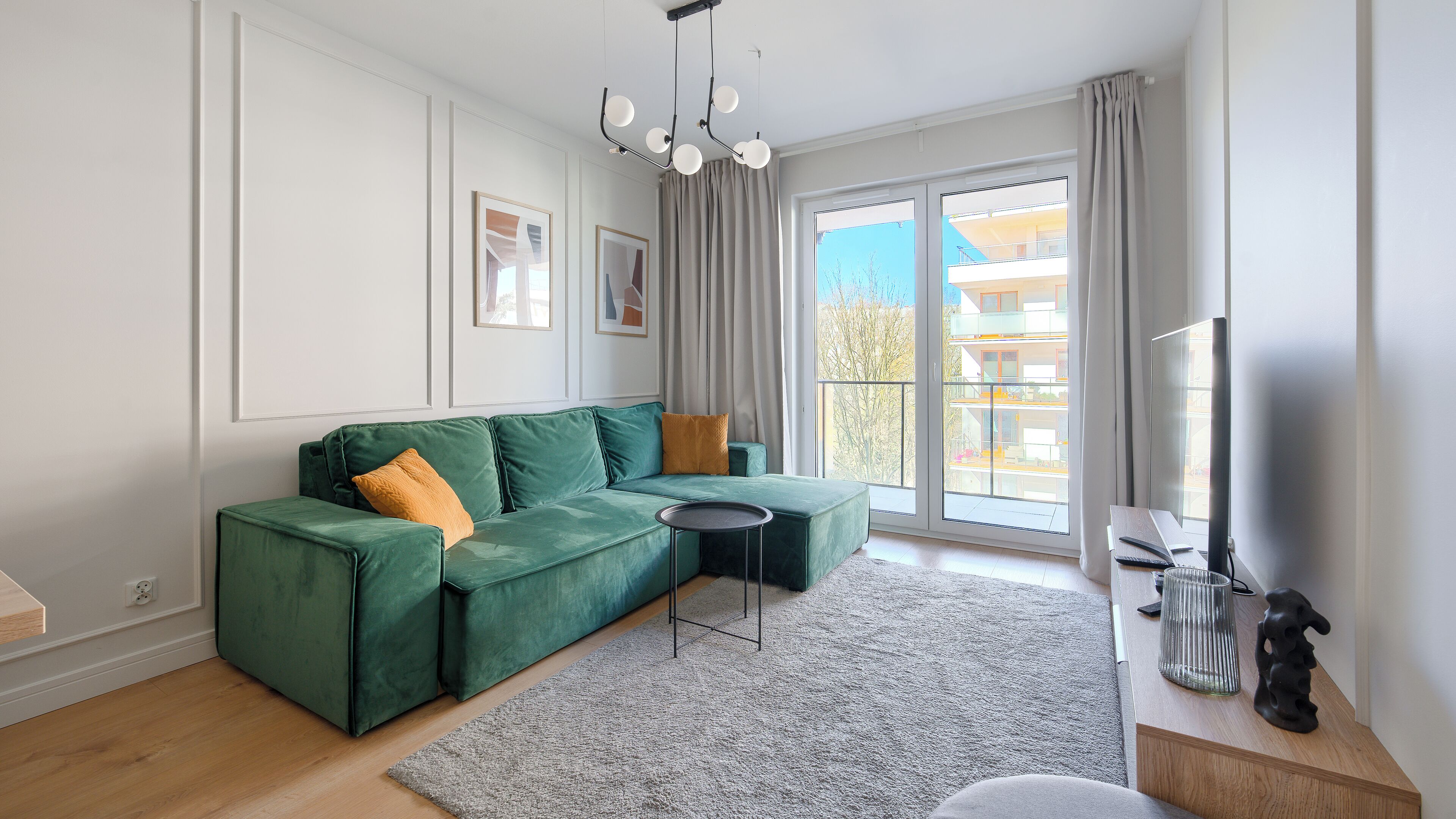 Ein modernes Wohnzimmer mit einem grünen Ecksofa, einem kleinen runden Tisch und einem großen Fenster mit Blick auf ein Gebäude.