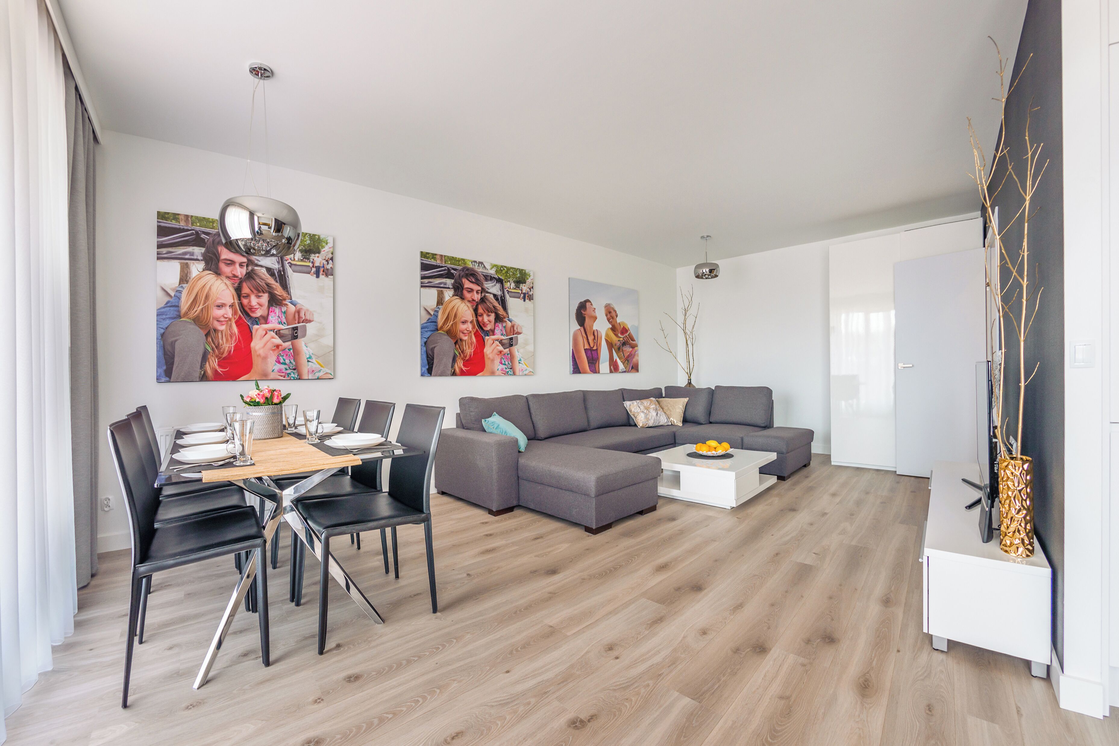 Een moderne woonkamer met een eetgedeelte, grijze banken, een witte salontafel en een eettafel gedekt voor vier personen.