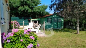 A green house with a red roof, a white chair, and purple flowers in the foreground. - Cozy Forest-Edge Vacation Home for 4 near Jard-sur-Mer (Saint-Vincent-sur-Jard)