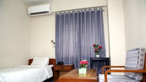 Ein Hotelzimmer mit Bett, Holztisch, Stuhl, Nachttisch, Lampe und Vorhang.