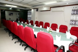 A conference room with a long table, red chairs, and white tablecloths. - Hotel Royal Palace (Dhaka)