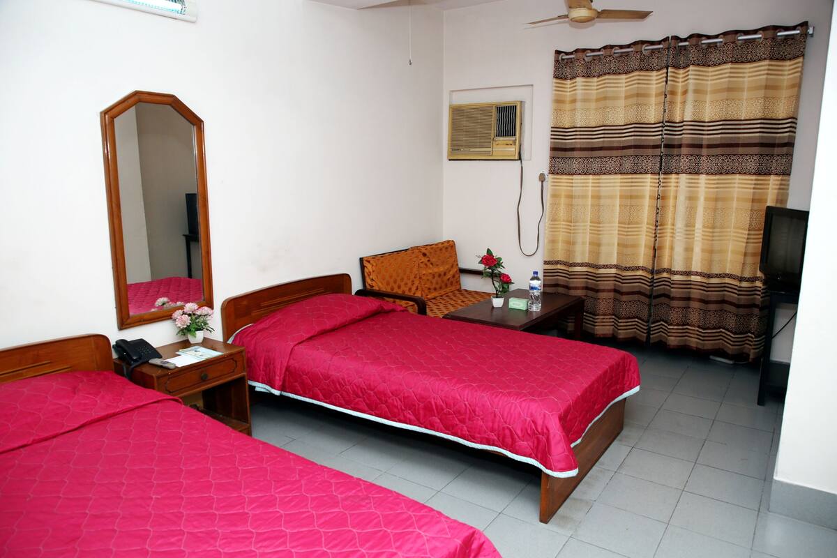 A hotel room with two single beds, a wooden nightstand, a mirror, a desk with a chair, a television, and a window with curtains.