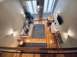 Un salón con techos altos, un sofá, una alfombra y suelo de madera.