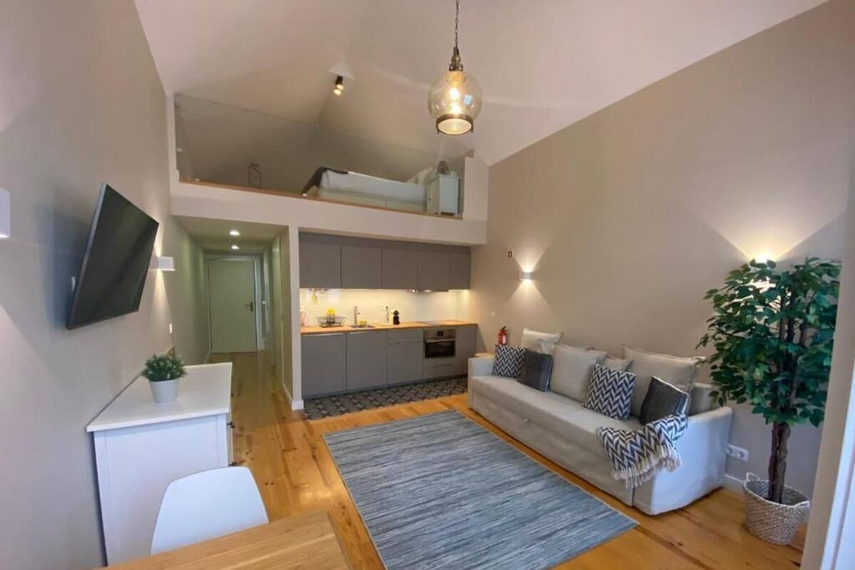 A modern apartment with a loft bedroom, a kitchen, a living area with a sofa and a dining table.