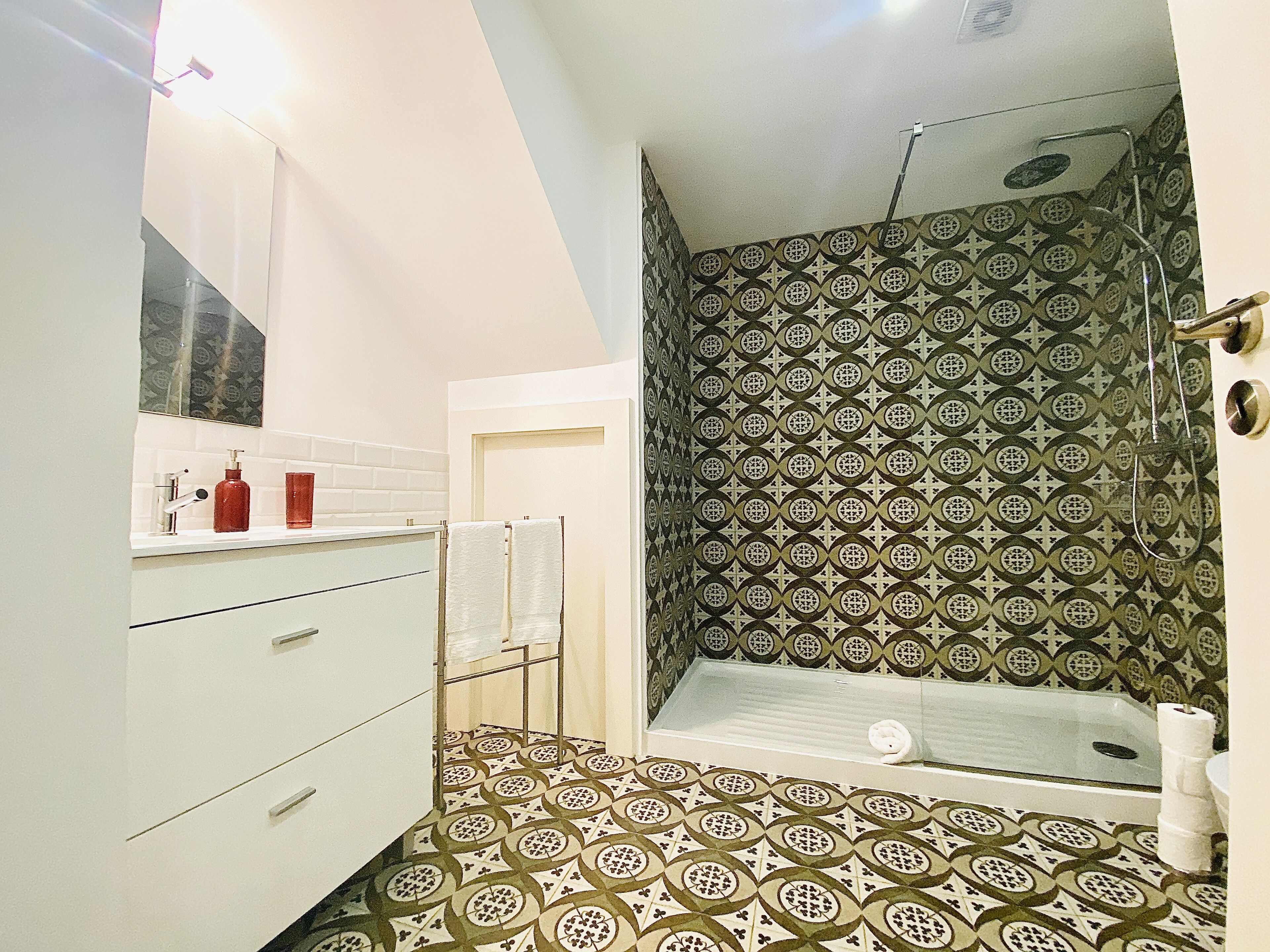 A bathroom with patterned tiles, a shower, a sink with a mirror, and a toilet.