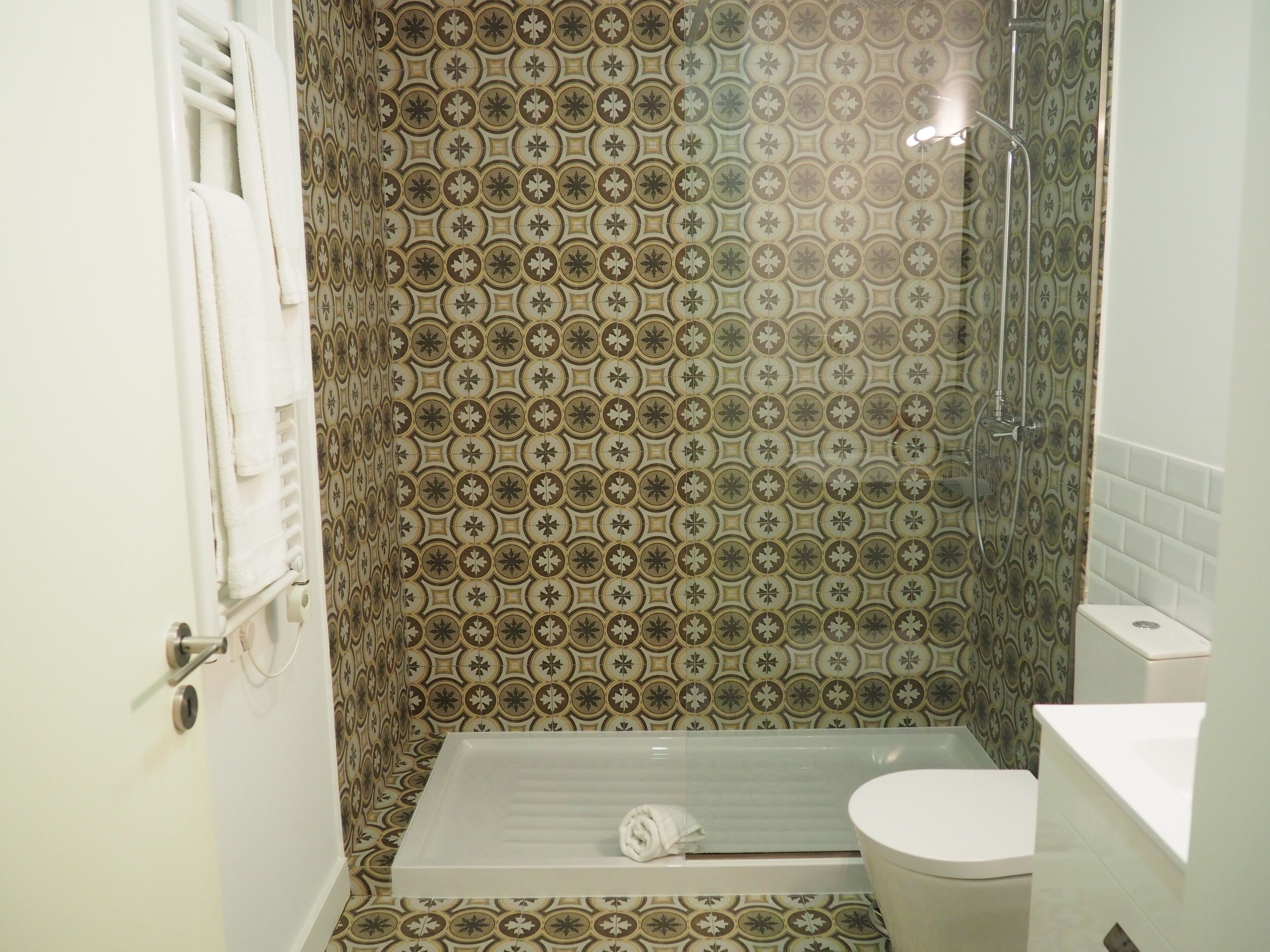 A bathroom with patterned tiles, a shower, a toilet, and a towel rack.