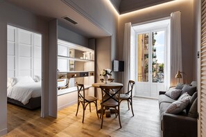 A modern living room with a wooden floor, a round dining table with chairs, a sofa, and a TV mounted on the wall.