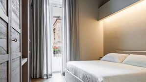Moderni hotellihuone, jossa on suuri sänky, puinen vaatekaappi ja näkymä kadulle.