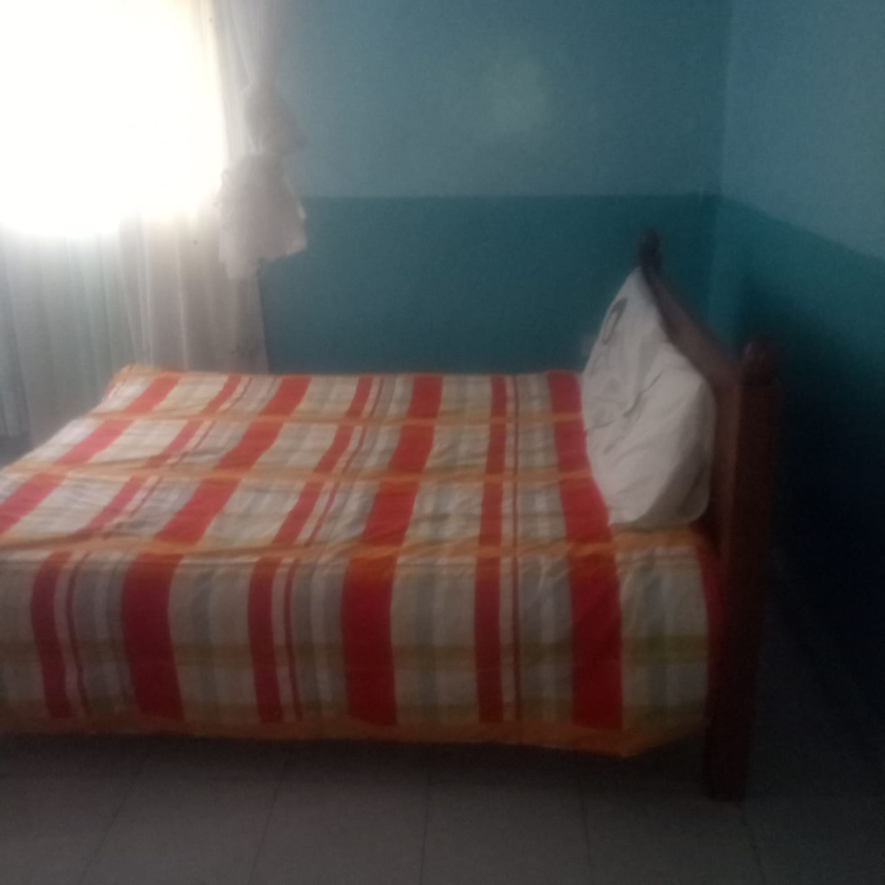 Una cama individual con colcha a rayas en una habitación con paredes color turquesa y una cortina blanca.