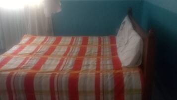 Una cama individual con colcha a rayas en una habitación con paredes color turquesa y una cortina blanca.