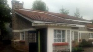 A two-story building with a tiled roof, a small porch, and a window with a decorative grille. - Reed Hotel Annex (Ongata Rongai)