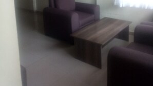 A living room with a sofa, a coffee table, and a TV mounted on the wall. - Reed Hotel Annex (Ongata Rongai)