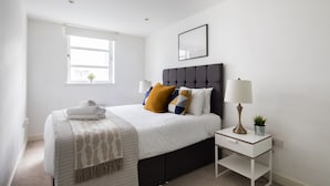 A neatly arranged bedroom with a bed, bedside table, lamp, and a small potted plant. - Elegant & Beautiful City Centre flat (London)