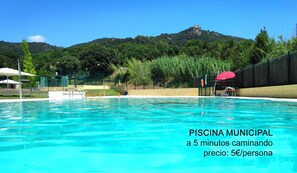 A municipal swimming pool with clear blue water, surrounded by a fence and greenery.