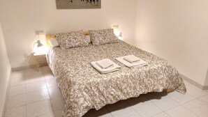 A neatly made bed with a patterned bedspread and two pillows, two folded towels on the bed, and a wall-mounted light fixture. - Ca la iaia - Village house in the old town of Amer (Amer)