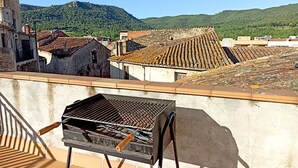 A rooftop terrace with a grill, a chair, and a view of a town with terracotta roofs and a mountain in the background. - Ca la iaia - Village house in the old town of Amer (Amer)
