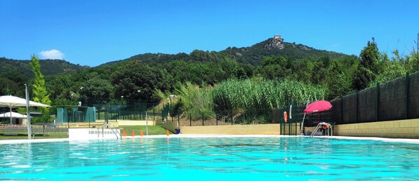 A municipal swimming pool with clear blue water, surrounded by a fence and greenery.
