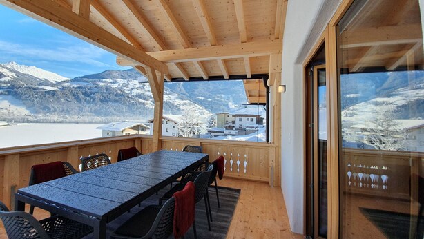 Una terraza de madera con una mesa y sillas, con vistas a un paisaje montañoso nevado.
