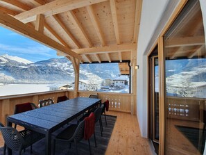 A wooden deck with a table and chairs, overlooking a snowy mountain landscape.