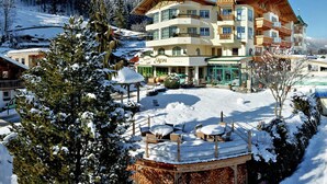 Ein mehrstöckiges Hotel mit Blick auf ein Skigebiet, inklusive Skilift, Sitzgelegenheiten im Freien und verschneiter Landschaft.