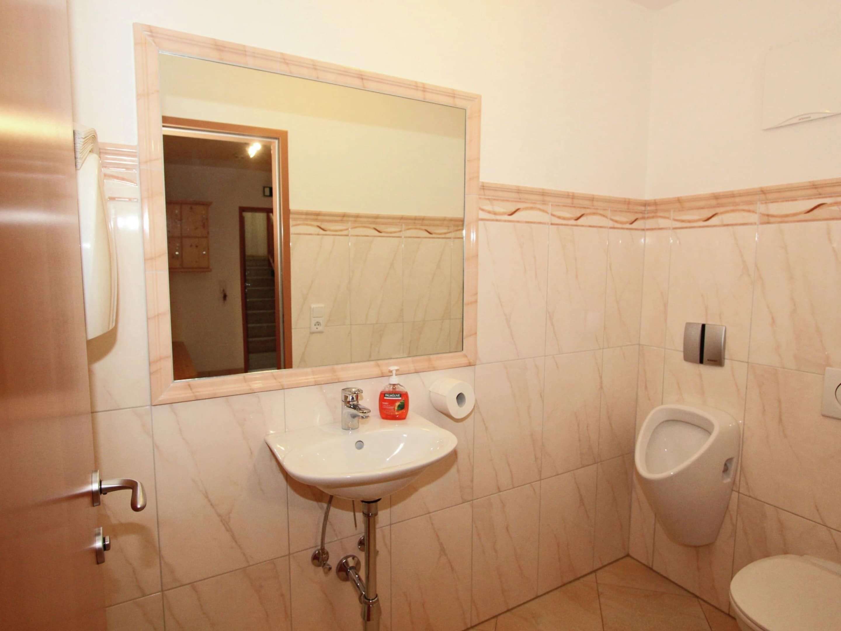 Une salle de bain équipée d’un lavabo, d’un miroir, d’un urinoir et de toilettes.