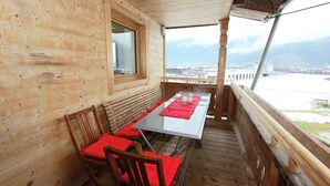 Una cabaña de madera con balcón, una mesa con sillas y vistas a un cuerpo de agua y edificios a la distancia.