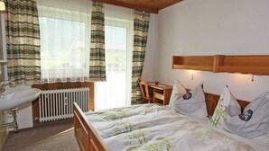 A bedroom with a wooden bed, a bedside table, a desk, a chair, a radiator, and a window with curtains. - Chalet in Aschau Near Ski Bus & Zillertal Slopes (Aschau Im Zillertal)