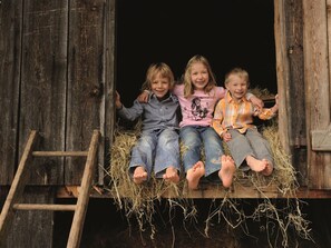 Three children sitting on hay in a wooden structure with a ladder.