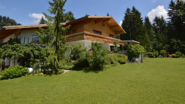A two-story wooden house with a sloped roof, surrounded by a well-maintained lawn and various trees. - Heavenly Apartment in Wängle Tyrol near Walking Trails (Waengle)