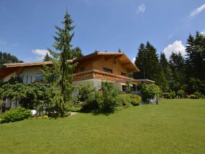 A two-story wooden house with a sloped roof, surrounded by a well-maintained lawn and various trees. - Heavenly Apartment in Wängle Tyrol near Walking Trails (Waengle)