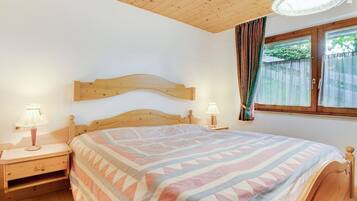 A bedroom with a wooden headboard, two bedside tables with lamps, a patterned bedspread, and a window with curtains.